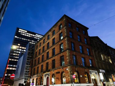 Manchester, İngiltere - 10 Aralık 2025: Manchester 'daki Gece Vakti Faulkner st şehir manzarası tuğla mimarisi ve modern gökdelenlerin arkasında.