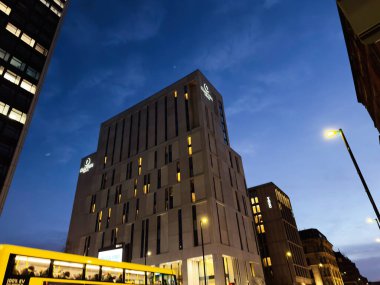 Manchester, İngiltere - 10 Aralık 2025: Sarı otobüsü ve ışıklı pencereli modern Clayton Hotel Manchester binasının akşam manzarası