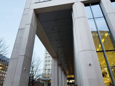 Geniş sütunları, cam panelleri ve kapalı bir yürüyüş yolu olan gösterişli bir şehir binası..