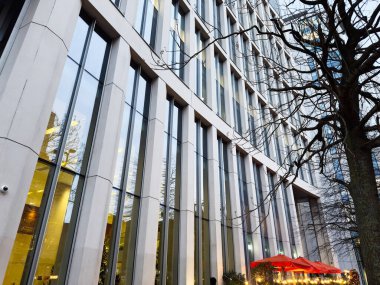 Manchester 'daki çağdaş bir ofis cephesinde cam paneller, sıcak iç aydınlatma ve açık hava oturma alanları yer alıyor..