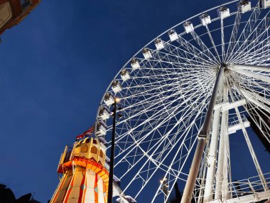 Manchester 'da alacakaranlıkta aydınlık bir kulenin yanında bir dönme dolabın parlak gece sahnesi..