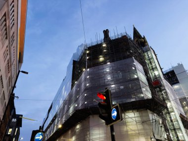 Manchester 'da inşaat alanı, iskele, cam cephe ve trafik ışıkları ile şehir caddesi boyunca alacakaranlıkta..