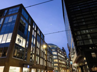 Manchester 'da akşam mavi saati işlek bir cadde boyunca cam ofisler ve yansımalar gösteriyor..