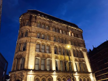 Manchester 'daki gece sahnesi sıcak ışıklarla yıkanmış tarihi bir taş binanın altını çiziyor..