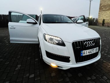 Kyiv, Ukrayna - 19 Aralık 2025: Parlak beyaz Audi Q7 ön ışıkları açık, iki kapı açık, akşam.