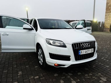 Kyiv, Ukrayna - 19 Aralık 2025: Premium beyaz Audi Q7 SUV açık kapılı, parke taşından bir yüzeye park edilmiş, açık ışıkların altında..