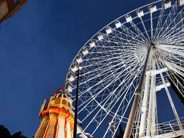 Manchester 'da alacakaranlıkta aydınlık bir kulenin yanında bir dönme dolabın parlak gece sahnesi..