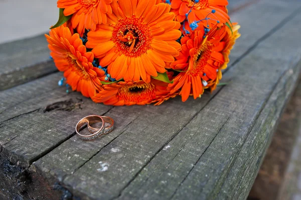 Orange wedding bouquet gerbera with rings at the wooden bench — Stock Photo, Image