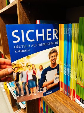 Londra, İngiltere - 12 Aralık 2025: Renkli ders kitapları ve arka plandaki öğrencilerin yanında ahşap bir rafta parlak mavi Almanca ders kitabı.