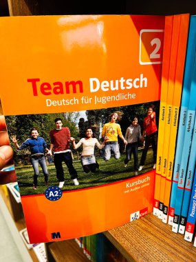 Londra, İngiltere - 12 Aralık 2025: Genç öğrenciler için parlak turuncu takım ders kitabı, parka atlayan bir grup çocuk.