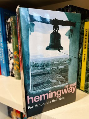 Londra, İngiltere - 12 Aralık 2025: Arka planda çan ve köy çatıları olan bir rafta klasik Hemingway romanı. Çanlar kimin için çalıyor?