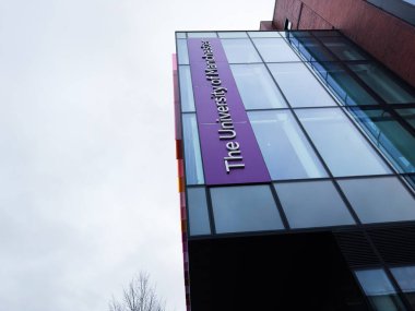 Manchester, İngiltere - Aralık 06, 2025: Manchester 'daki modern cam üniversite binasında mor dikey bir pankart ve kentsel mimari.