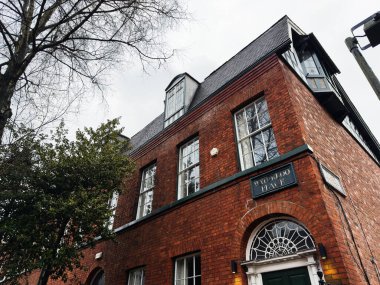 Manchester, İngiltere - Aralık 06, 2025: Manchester kentsel cephesi kırmızı tuğlalı, zamansız mimari, kemerli kapı ve ağaçlarla kaplı sokak.