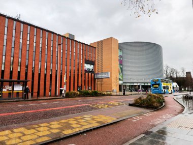 Manchester, İngiltere - Aralık 06, 2025: Manchester 'da kavisli gümüş binası, mavi otobüsü ve yayaları olan çağdaş üniversite dışı.