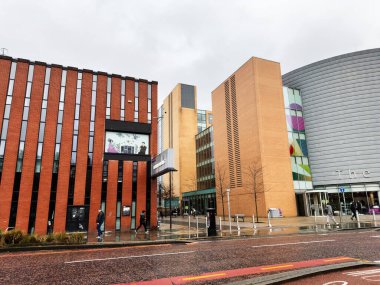 Manchester, İngiltere - 06 Aralık 2025: Manchester 'da şehir sahnesi tuğla mimarisi, cam paneller ve ıslak bir cadde boyunca yürüyen insanları gösteriyor.