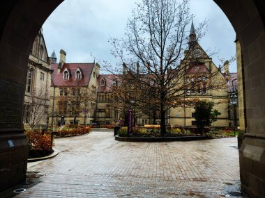 Manchester, İngiltere - 06 Aralık 2025 Manchester 'da sakin bir üniversite avlusu taş kemer, tuğla patika ve çıplak ağaçlarla çevrili.