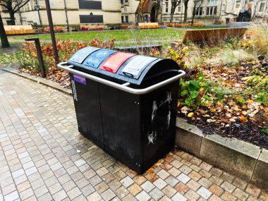 Manchester, İngiltere - Aralık 06, 2025: Manchester parkında kamu atığı ve geri dönüşüm kutusu, sonbahar tonları, banklar ve bahçe yatakları.