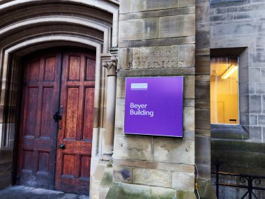 Manchester, İngiltere - Aralık 06, 2025: Manchester 'da taş bina kemerli ahşap kapı ve mor Charles Beyer Binası işareti, şehir kampüsü titreşimi.