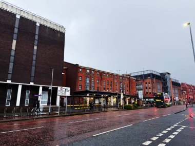 Manchester, İngiltere - 06 Aralık 2025: Manchester 'da yağmurlu şehir manzarası bir otobüs, tuğla binalar ve sakin bir sokak.