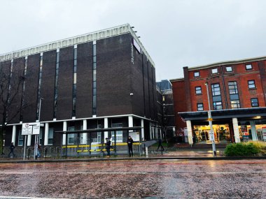 Manchester, İngiltere - Aralık 06, 2025: Manchester, İngiltere 'de yağmurlu şehir caddesi, tuğla binalar, bir otobüs durağı ve bir dizi dükkan.