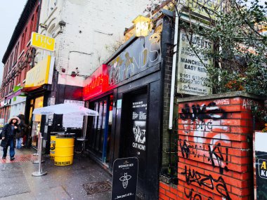 Manchester, İngiltere - Aralık 06, 2025: Yağmurlu bir günde Manchester sokak vitrinlerinde neon ışıkları, grafiti duvarları ve açık havada oturma.