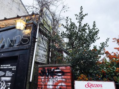 Manchester, İngiltere - Aralık 06, 2025: Manchester 'da bir sokak sahnesinde bir kafe, grafiti duvarı, bitkiler ve bir Rizzo tabelası yer alıyor.