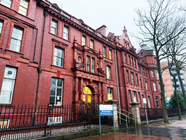 Manchester, İngiltere - Aralık 06, 2025: Manchester 'da kemerli giriş, demir çit ve klasik mimari içeren tarihi kırmızı tuğla bina.