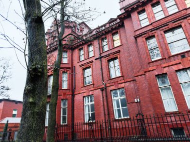 Manchester, İngiltere - Aralık 06, 2025: Manchester 'daki kırmızı tuğla bina büyük pencerelere ve ağaç kaplı bir sokak boyunca dekoratif demir çitlere sahiptir.