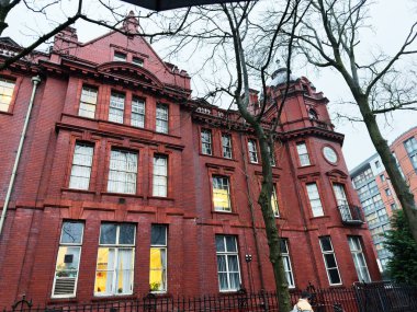 Manchester, İngiltere - Aralık 06, 2025: Manchester 'daki tarihi kırmızı tuğla bina büyük pencereler, saat kulesi ve sıcak iç ışıklar içeriyor.