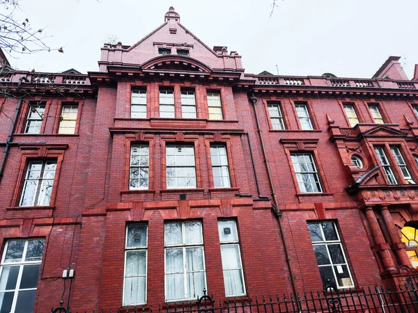 Manchester, İngiltere - Aralık 06, 2025: Manchester UK 'de uzun kuşak pencereleri ve dekoratif mimari detayları bulunan kırmızı tuğla bina.