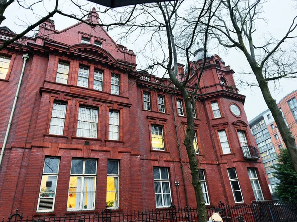 Manchester, İngiltere - Aralık 06, 2025: Manchester 'daki tarihi kırmızı tuğla bina büyük pencereler, saat kulesi ve sıcak iç ışıklar içeriyor.