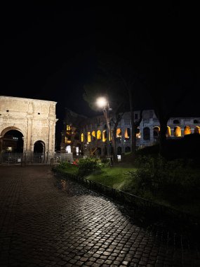 Roma, İtalya - 23 Temmuz 2025: Süslü bir kemerin ve yanan bir oyun salonunun yer aldığı sakin bir gece sahnesi.