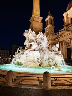 Roma, İtalya - 29 Temmuz 2025: Heykeller, su ve kilise mimarisinin parladığı büyük bir Barok çeşmesinin gece sahnesi. Fontana dei Quattro Fiumi
