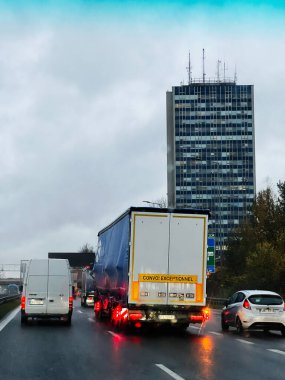 Katowice, Polonya - 29 Kasım 2025: Yüksek bir binanın yanındaki kalabalık bir otoyolda nakliye kamyonu, yansıtıcı ışıklarla dolu yağmurlu bir gün.
