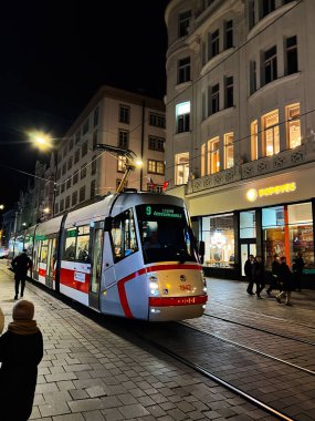 Brno, Çek Cumhuriyeti - 29 Kasım 2025: Yoğun bir Brno şehrinde modern bir tramvayın gece sahnesi, vitrinlerden parlıyor