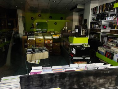 Brno, Çek Cumhuriyeti - 29 Kasım 2025: Plak rafları, sandıklar ve parlak yeşil bir aksan duvarının yer aldığı loş ışıklı bir plak mağazası sahnesi.