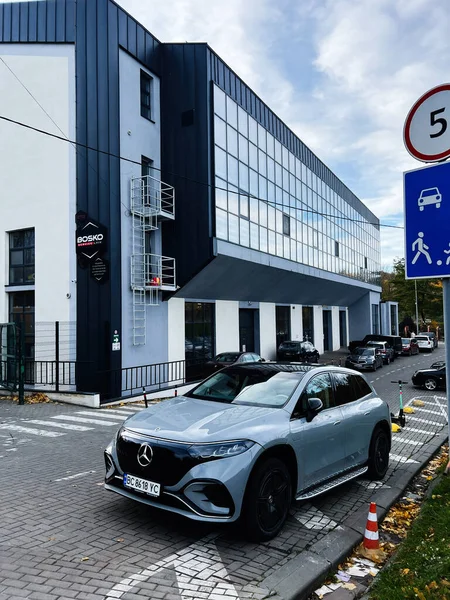 Lviv, Ukrayna - 03 Kasım 2025: Şık bir Mercedes-Benz EQS SUV arabası şehir caddesi boyunca uzanan çağdaş mavi camdan bir binanın yanında.