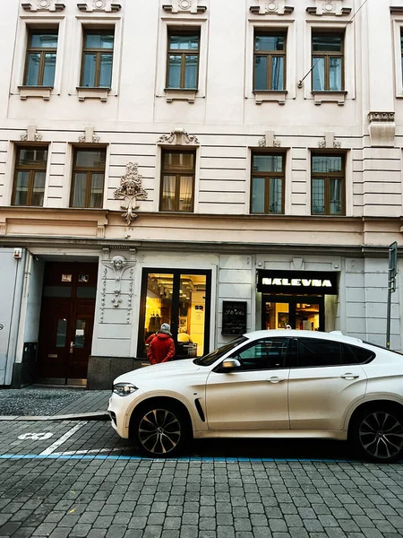 Brno, Çek Cumhuriyeti - 29 Kasım 2025: Brno yakınlarında bir yaya ve kaldırım taşı caddesi boyunca park etmiş beyaz bir SUV ile şehir vitrini sahnesi.