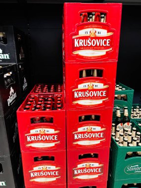 Brno, Çek Cumhuriyeti - 29 Kasım 2025: Parlak kırmızı sandıklar bir mağaza rafında bira şişelerini tutarak cesur bir Kruovice birası gösterisi yarattılar.