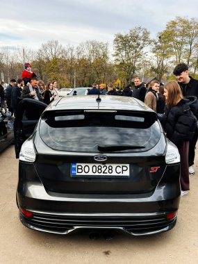Ternopil, Ukrayna - 29 Kasım 2025: Siyah bir Ford Focus ST hatchback 'in etrafında arka planda ağaçlarla birlikte bir kalabalık toplandı.