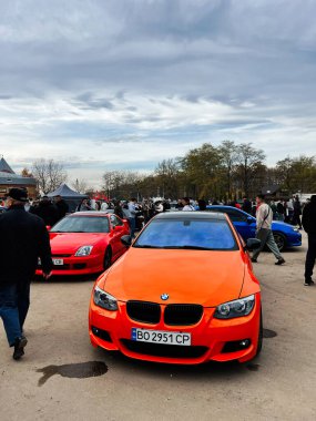 Ternopil, Ukrayna - 29 Kasım 2025: Turuncu bir BMW 3 serisi E93 serisi etrafında toplanan kalabalık arka planda diğer renkli arabalarla birlikte bir açık hava otomobil fuarında.