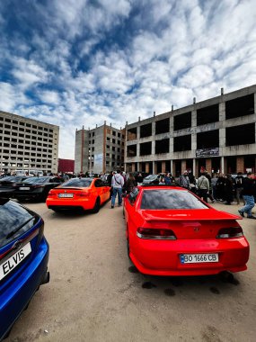 Ternopil, Ukrayna - 29 Kasım 2025: İnsanlar arka planda tamamlanmamış binalar görünürken parlak kırmızı ve turuncu arabaların yakınında kaynaşıyorlar.