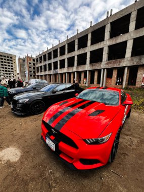 Ternopil, Ukrayna - 29 Kasım 2025: Kalın siyah çizgili parlak kırmızı Mustang şehir inşaatı, arabalar ve seyirciler arasında duruyor.