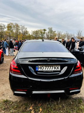 Ternopil, Ukrayna - 29 Kasım 2025: Parlak siyah Mercedes-Benz S-Sınıfı Brabus W222 sedan yakınlarda kalabalık ve Ukrayna plakalı bir açık hava araba fuarında.