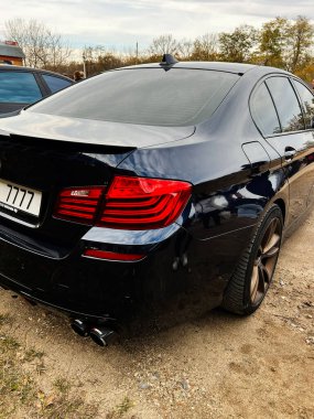 Ternopil, Ukrayna - 29 Kasım 2025: Parlak siyah BMW M5 F10 sedan, arka ışıklar, spoiler ve yansımalar göstermektedir..