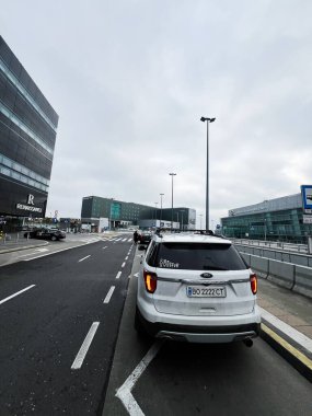 Varşova, Polonya - 29 Kasım 2025: Beyaz bir Ford Explorer SUV Varşova 'daki modern havaalanı binalarının yanındaki işlek bir şehir yolu boyunca park etti.