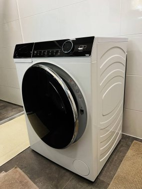 Öndeki parlak çamaşır makinesi temiz beyaz kiremitlerle temiz bir çamaşırhanede duruyor..