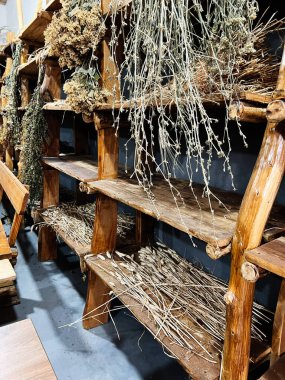 Ahşap raflar, kurumuş otlar ve samanların alt katlara saçıldığı taşralı depolama sahnesi.