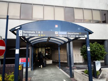 Manchester, İngiltere - 12 Ocak 2026: İnsanlar kalkış ve pikap işaretlerinin rehberliğinde mavi bir tepe örtüsünün altındaki modern Manchester havaalanı terminaline doğru yürüyorlar.