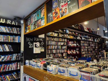 Manchester, İngiltere - 21 Ocak 2026: Sandıklar dolusu vinil, raflar dolusu albüm ve şimdi çalan bir karatahta tabelasıyla hareketli bir plak dükkanı sahnesi.